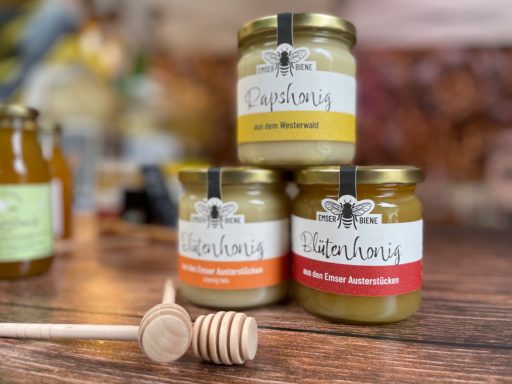 Drei Sorten Emser Biene Honig mit einem davor liegenden Honiglöffel